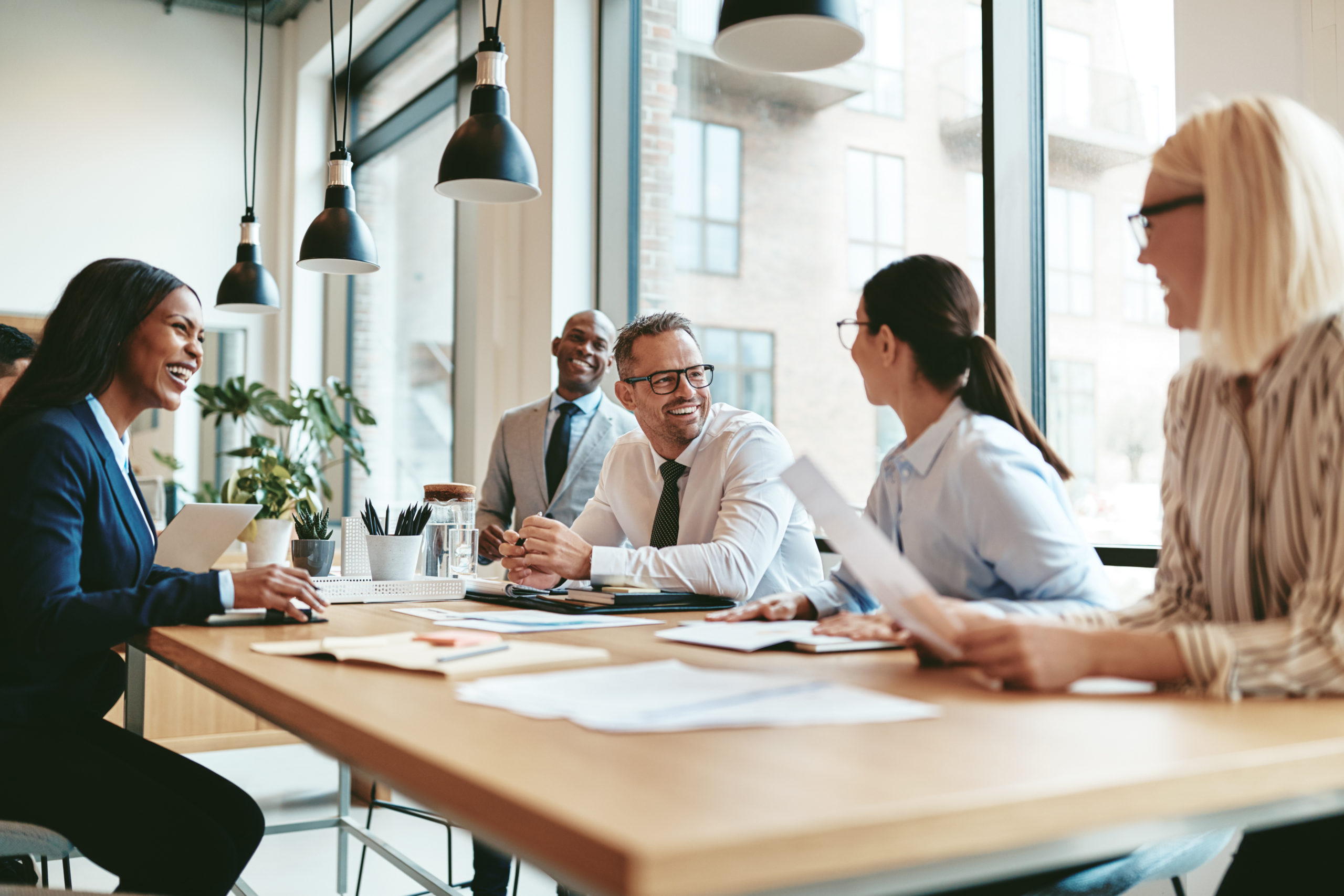 Diverse businesspeople laughing during a meeting around an offic diverse businesspeople meeting around a rectangular conference table