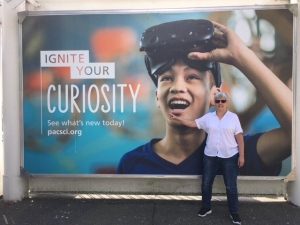 Sue standing next to a sign that says "Ignite Your Curiosity"