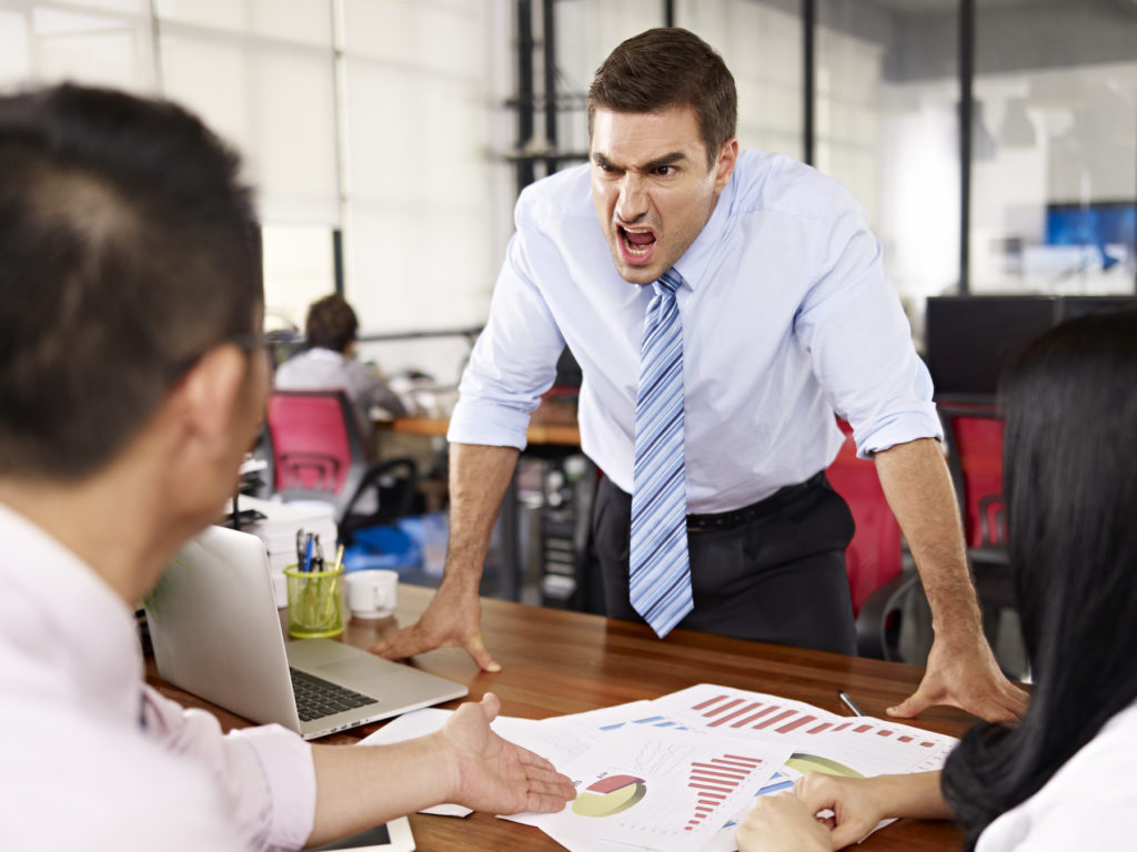 bad-tempered caucasian business executive yelling at two asian subordinates in office.